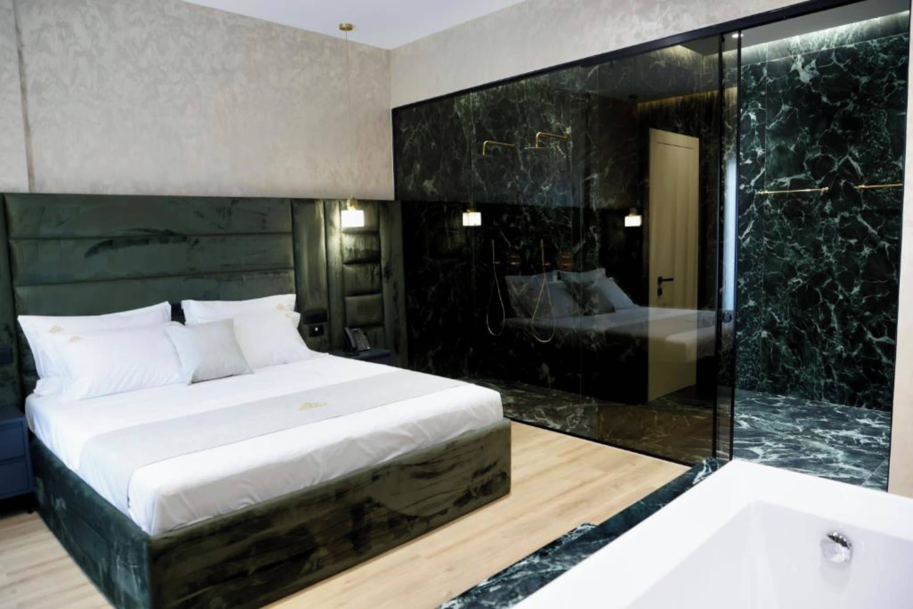 A modern bedroom with a large bed, a glass-enclosed bathroom, and a marble wall.