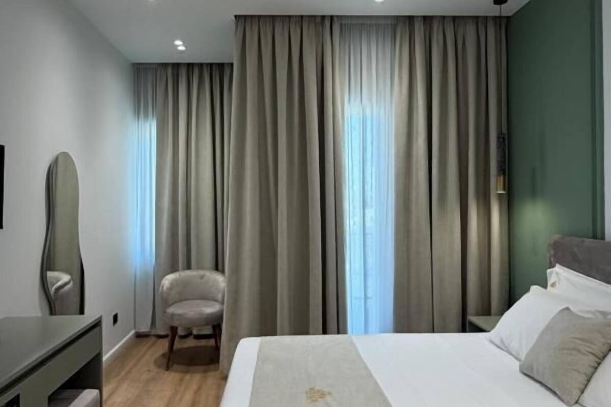 Una habitación de hotel con cama, escritorio, silla y un ventanal con cortinas.