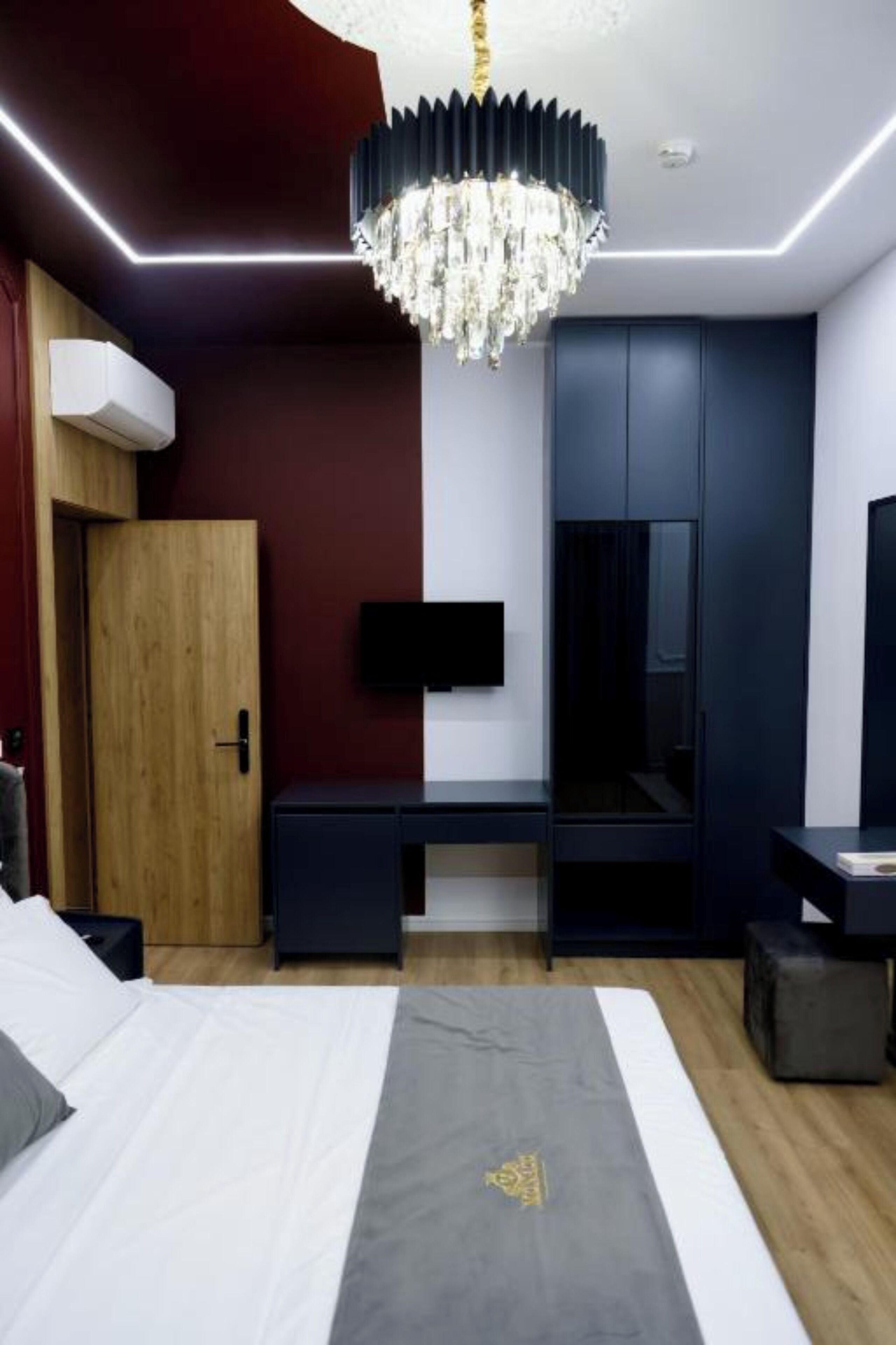 Een moderne slaapkamer met een bed, nachtkastje, kledingkast en een aan de muur bevestigde televisie.