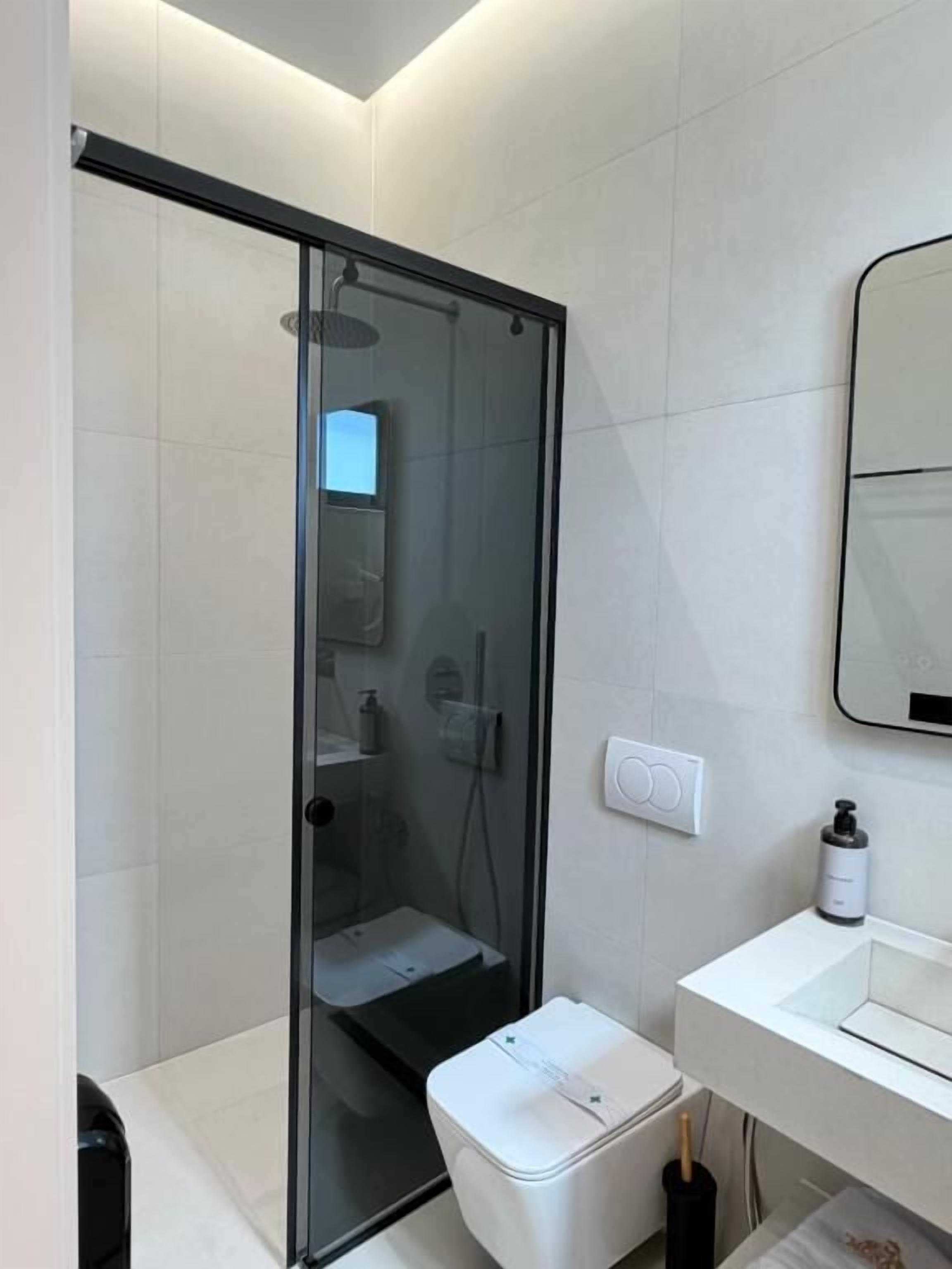 Un baño moderno con ducha de vidrio, lavamanos blanco y un inodoro.