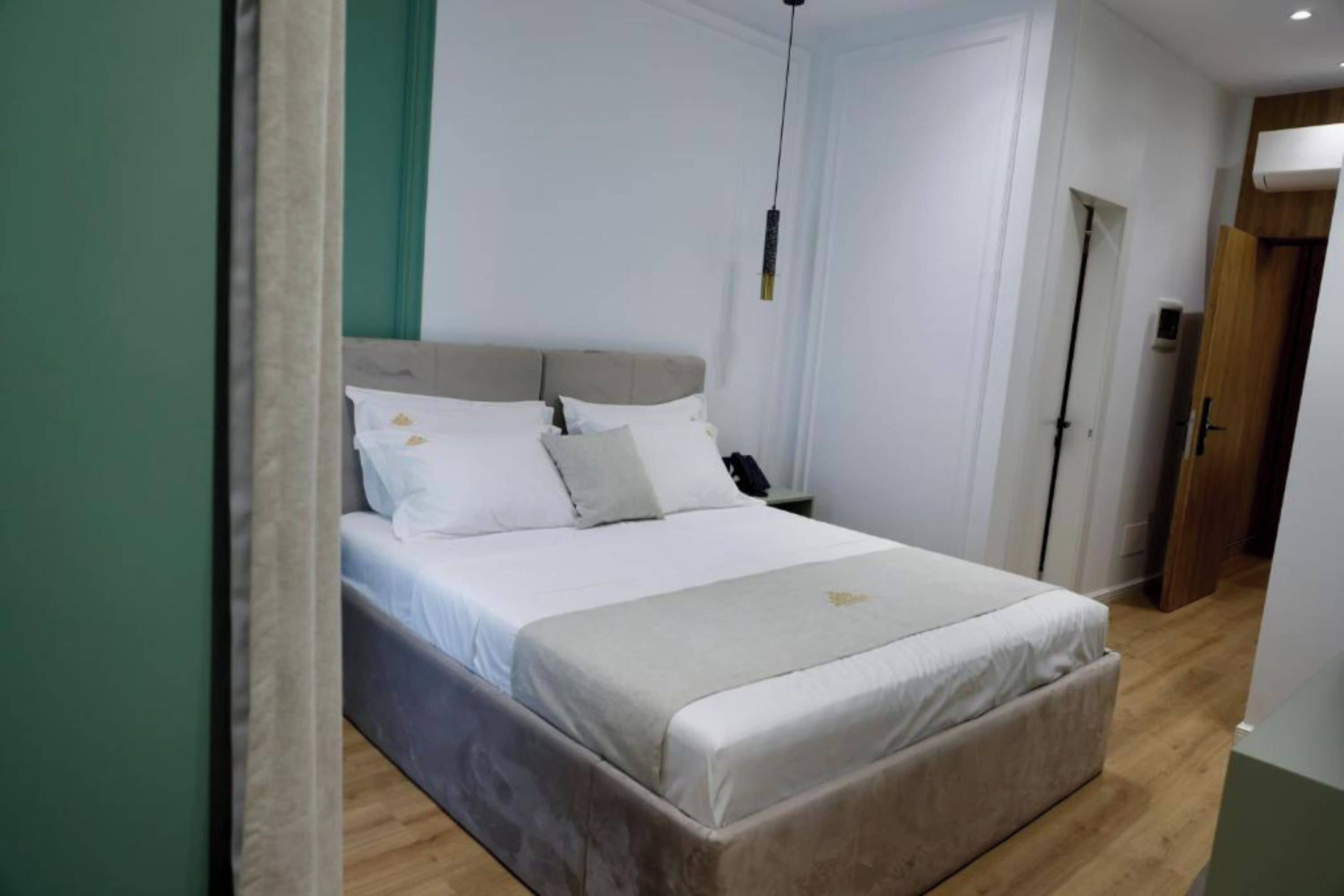 A bedroom with a bed, a bedside table, a hanging light fixture, and a door.