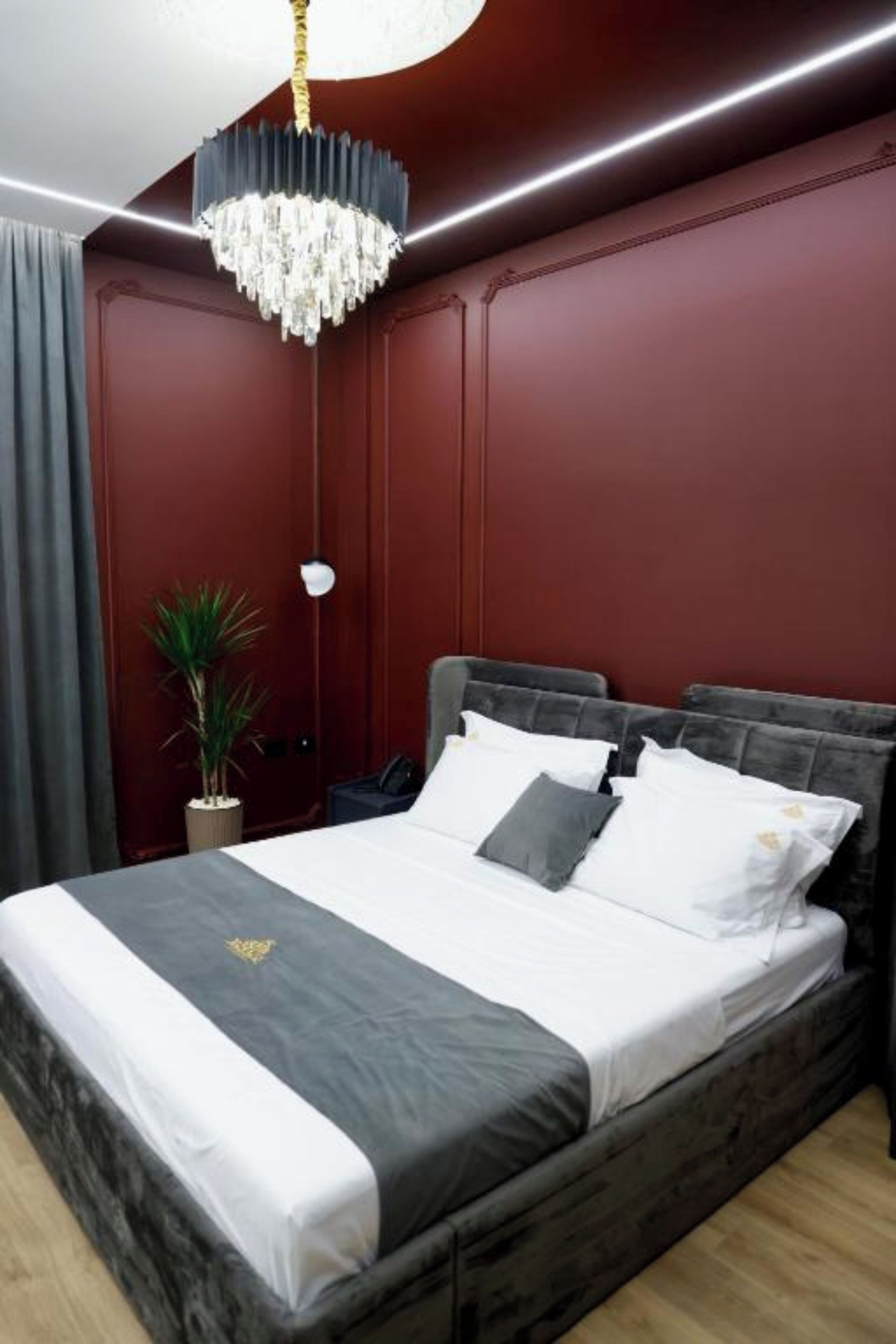 Un dormitorio con una cama grande, una araña, una planta en maceta y una pared de color rojo oscuro.