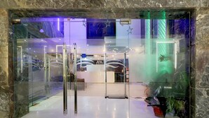 Una entrada de hotel moderna con puerta de cristal, un mostrador de recepción y una escalera visible.