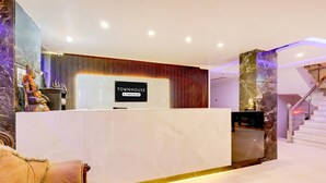 Un mostrador de recepción con un cartel que dice 'TOWNHOUSE Company Service', un pilar de mármol y una escalera.