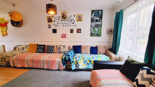 A cozy room with a sofa set, a wall with framed photos, and a decorative hanging light fixture. - Room-cosy Private Room in Family Home ne (London)