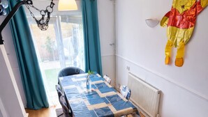 A room with a bed, a table with a quilt, a wall-mounted lamp, a radiator, and a window with curtains. - Room-cosy Private Room in Family Home ne (London)