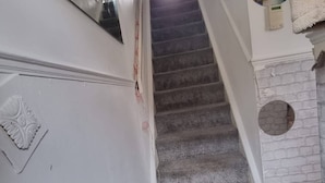 A staircase with a carpeted landing, a white wall with a decorative emblem, and a brick wall with a circular window. - Room-cosy Private Room in Family Home ne (London)