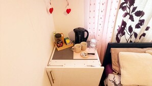 A small room with a kitchenette, a bed with a deer print bedspread, a window with a curtain, and a wall with heart decorations. - Room-cosy Private Room in Family Home ne (London)