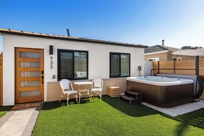 Una casa moderna con jacuzzi, un patio con sillas y un césped bien cuidado.