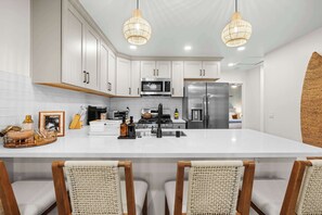 Una cocina moderna con armarios blancos, electrodomésticos de acero inoxidable y una isla central con taburetes de bar.