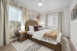 Un dormitorio con cama, cortinas, ventilador de techo y un mural de palmera en la pared.