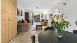 A modern living room with a sofa, armchairs, a coffee table, and a dining table with a vase of flowers. - Canalside Hideaway in Berkhamsted - Pass the Keys (Berkhamsted)