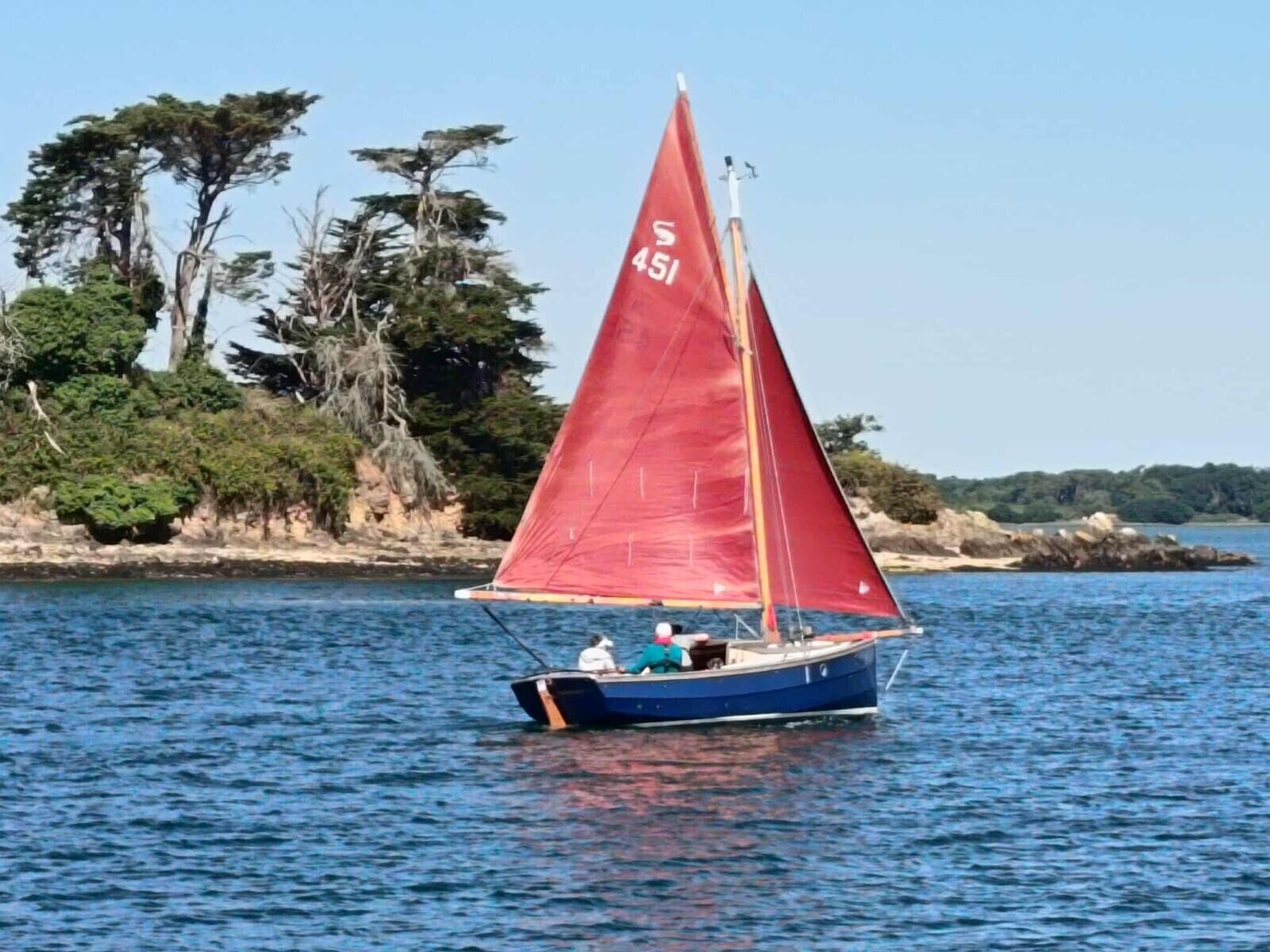 Een zeilboot met een rood zeil op een rustig wateroppervlak.