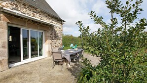 A stone building with a patio area, a table with chairs, and a glass door.