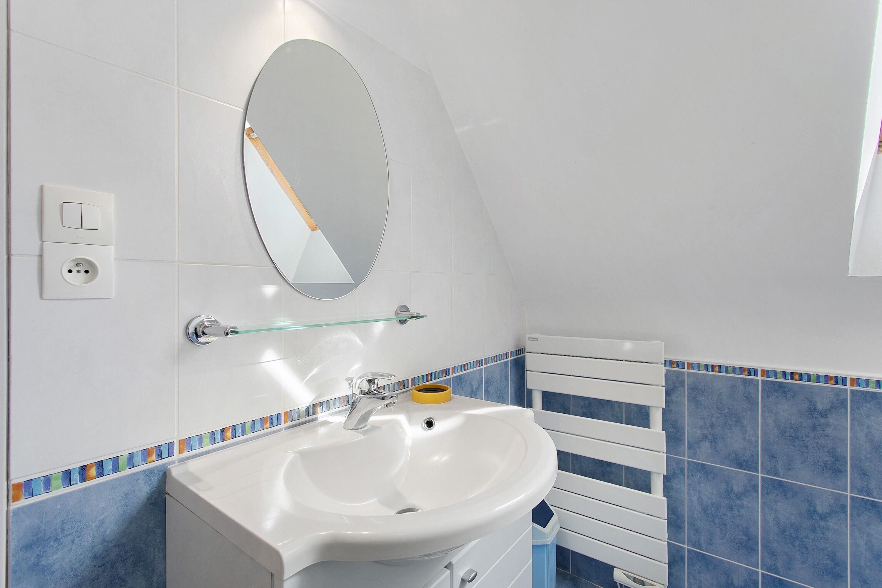 A bathroom with a white sink, a mirror, a glass shelf, and a towel rack.