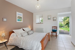 Une chambre à coucher comprenant un lit, une table de chevet, une lampe, une chaise et une vue dégagée sur l’extérieur grâce à une grande fenêtre.