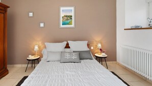 A bedroom with a bed, two bedside tables with lamps, a framed picture on the wall, and a radiator.