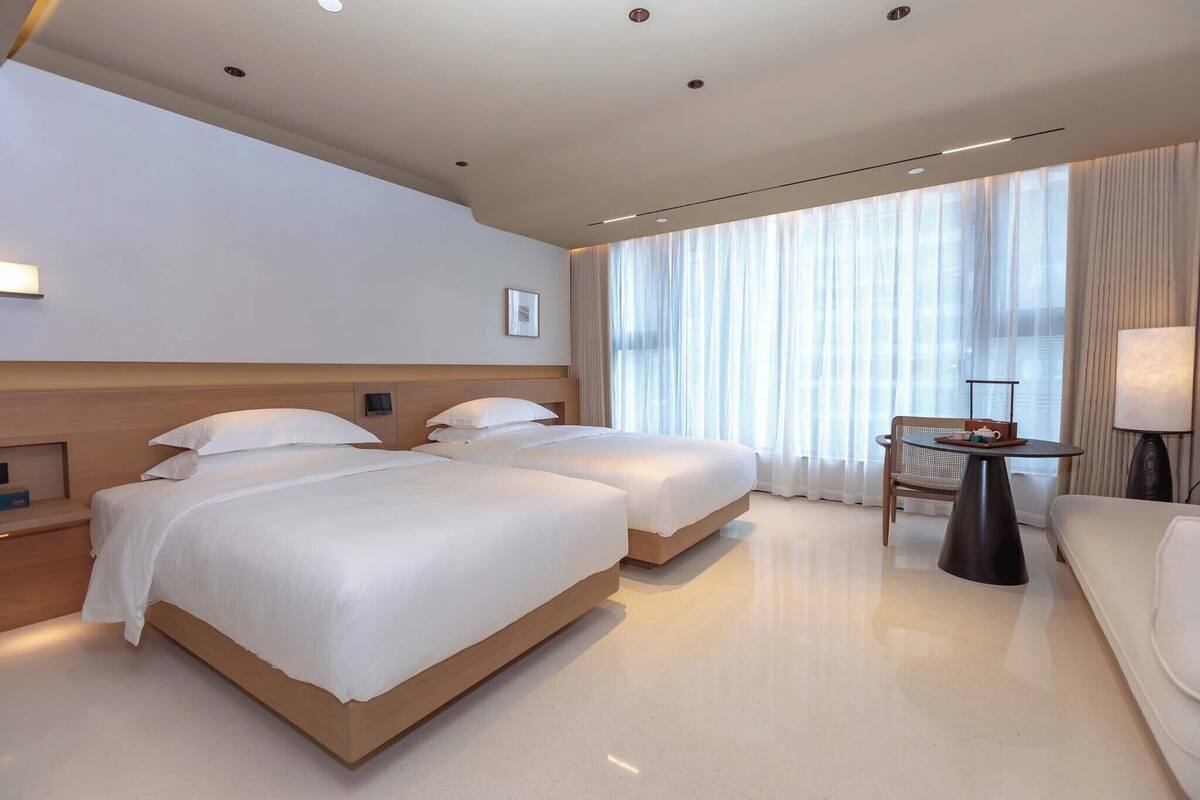 A hotel room with two beds, a small table, a chair, and a sofa.