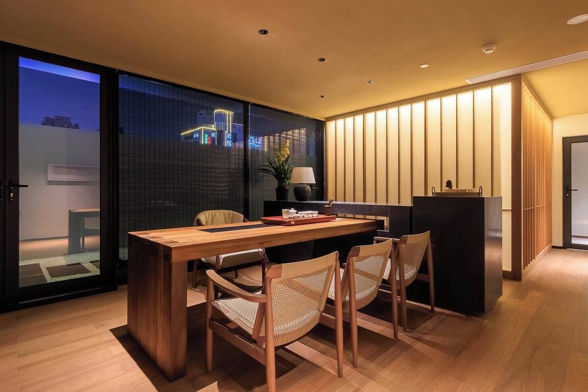 A modern dining area with a wooden table and chairs, a black cabinet, and a view of a cityscape through a glass door.
