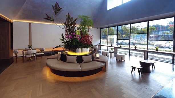 A modern lobby with a round seating area, a central plant arrangement, and large windows offering a view of the street. - Zhuhai Xumeishan Hotel  (Zhuhai)