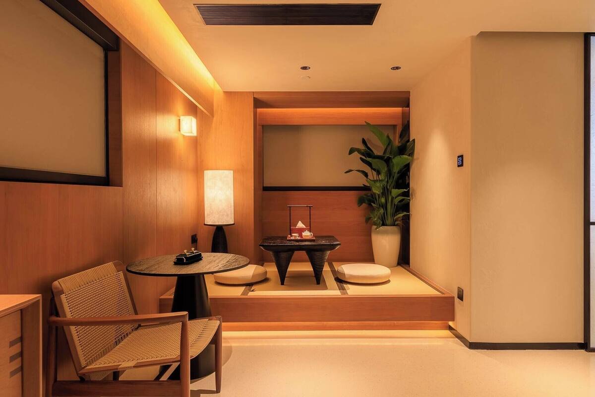 A modern hotel room with a wooden accent wall, a round table with a lamp, a sofa, and a potted plant.