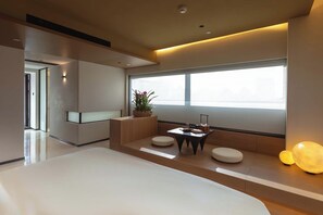 Une chambre d’hôtel moderne avec un grand lit, une petite table ornée d’un vase et un coin salon avec des coussins.