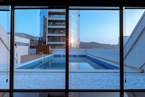 Une piscine intérieure moderne offrant une vue sur un immeuble de grande hauteur et un paysage vallonné.