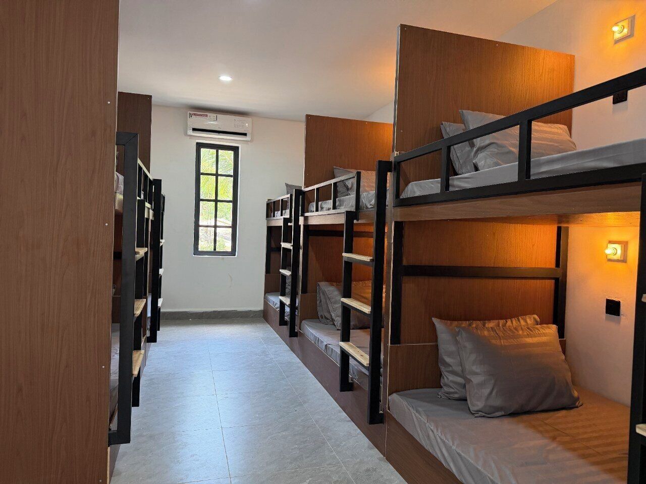 A dormitory room with bunk beds, a window, and an air conditioning unit.