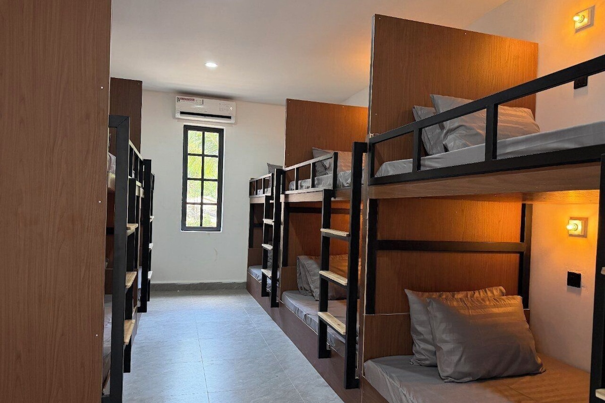 A dormitory room with bunk beds, a window, and an air conditioning unit.