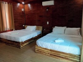 Una habitación con dos camas de madera, suelo de madera, pared de ladrillo y un equipo de aire acondicionado.