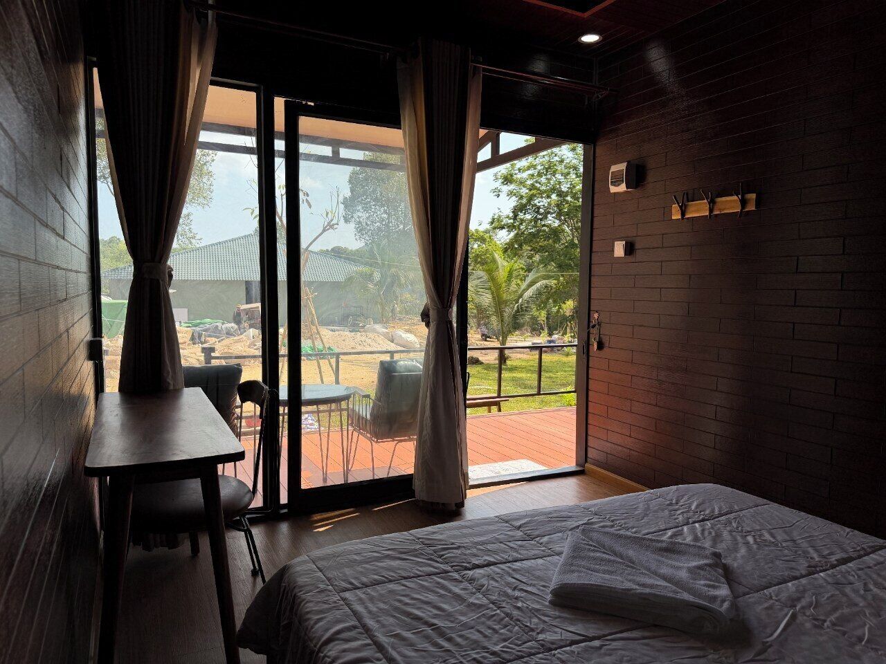 A room with a bed, a table, and a view of an outdoor area with a patio and chairs.