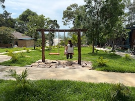 A person on a swing in a park with a stone pathway, greenery, and a building in the background.