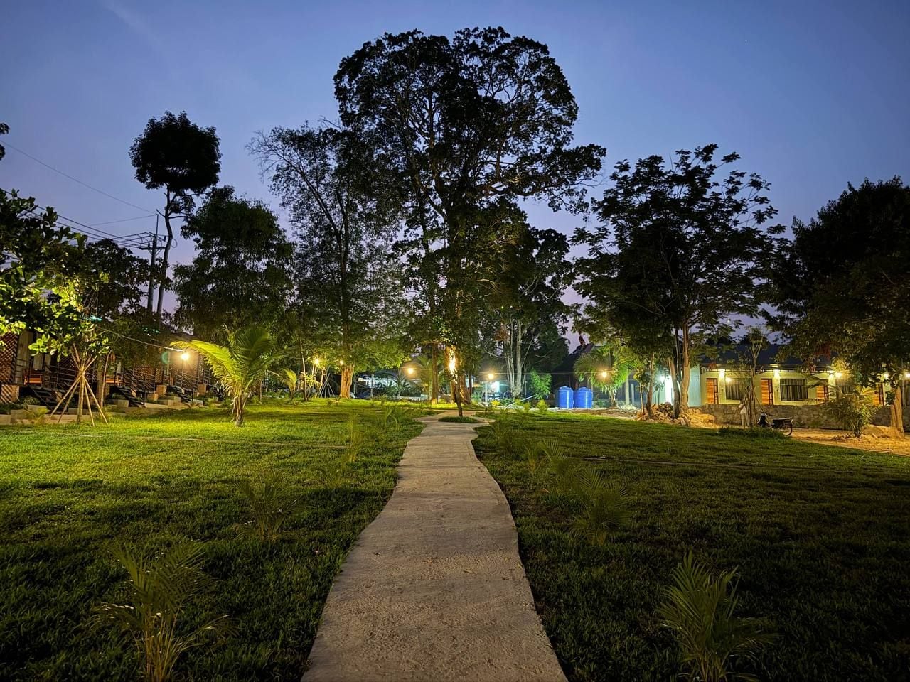 A nighttime outdoor area with a paved walkway, trees, and illuminated structures.