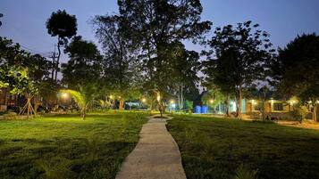 A nighttime outdoor area with a paved walkway, trees, and illuminated structures.