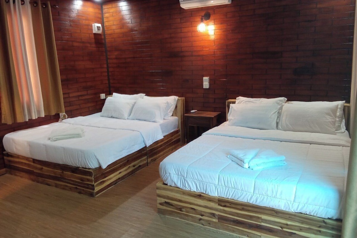 Two wooden beds with white bedding, a wooden floor, a brick wall, and a wall-mounted light fixture.