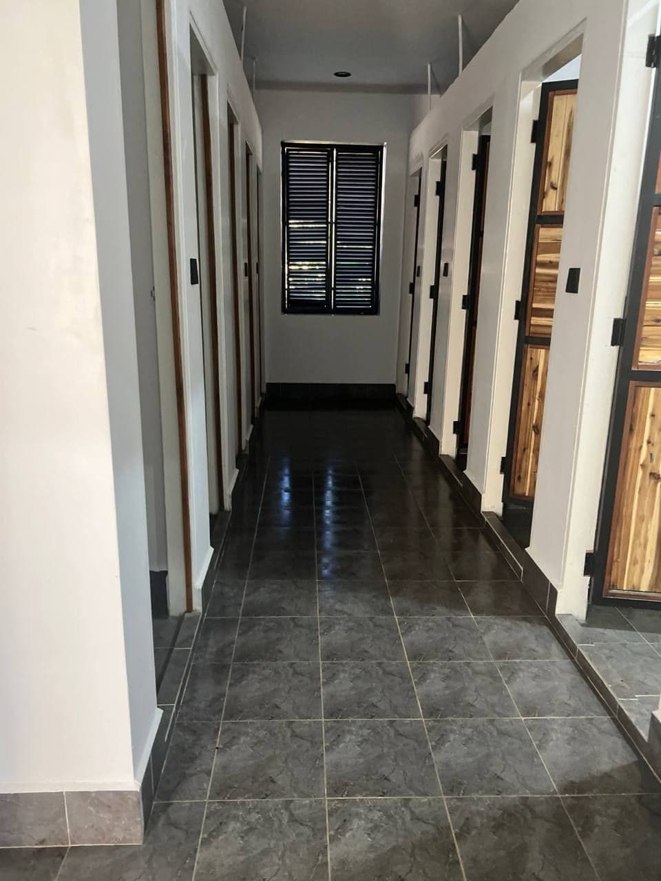 A corridor with dark tiled flooring and wooden doors on both sides.
