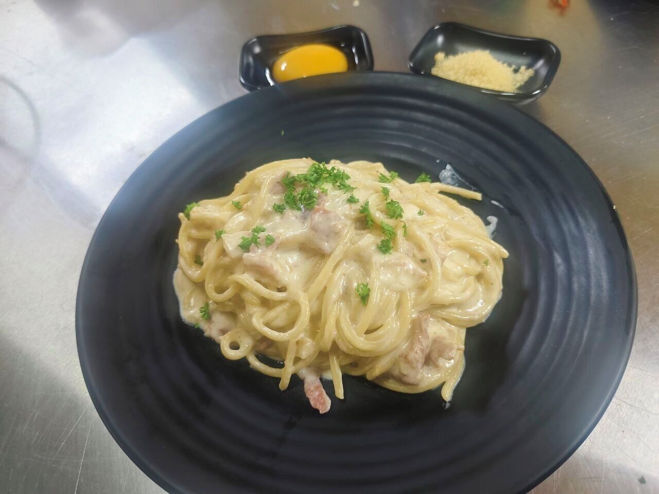 A plate of spaghetti with a creamy sauce, garnished with parsley, on a black plate.