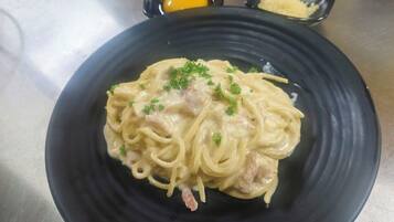 A plate of spaghetti with a creamy sauce, garnished with parsley, on a black plate.