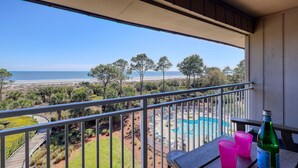 Een balkon met uitzicht op een strand, een zwembad en een fles.