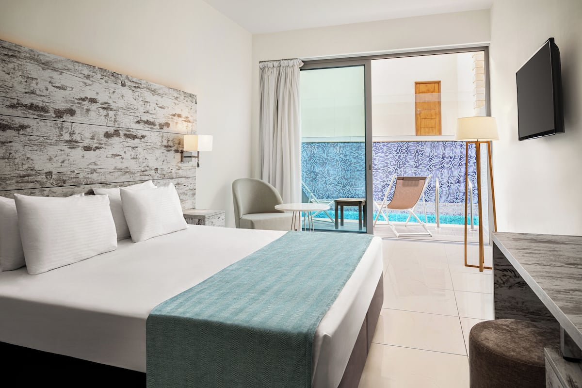 Habitación de hotel con cama, escritorio, silla, televisión y vista a la piscina.