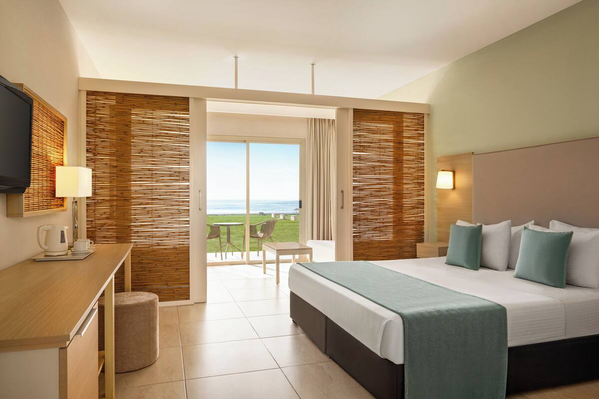 Habitación de hotel con cama, escritorio, silla, mesita y vistas al exterior.