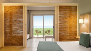 Una camera d'albergo con un letto, vista sul mare e un balcone con sedie.