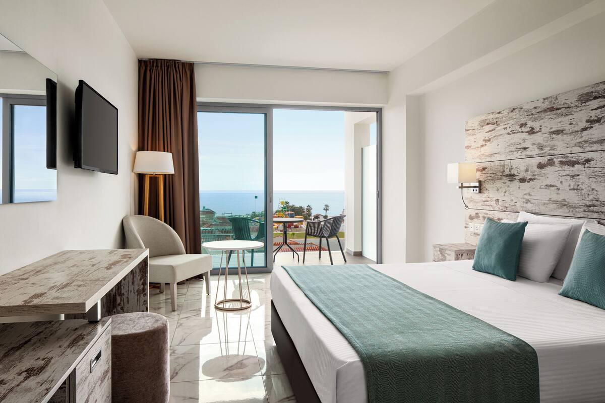 Una habitación de hotel moderna con una cama grande, un escritorio, una silla, una mesita y un balcón con vistas.