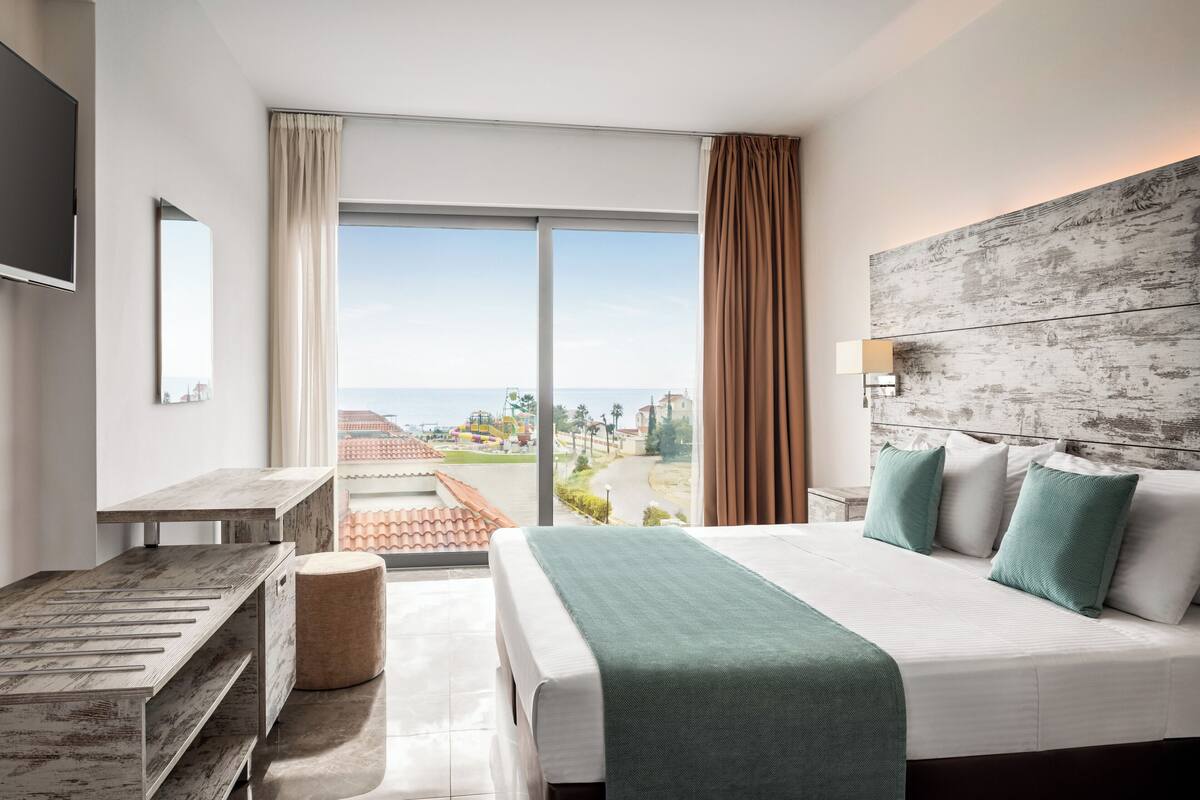 Habitación de hotel con cama, escritorio, ventana grande y vista a la ciudad.
