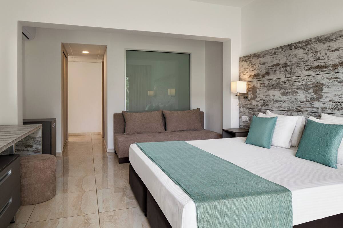 Habitación de hotel moderna con una cama grande, un sofá, un escritorio y vistas al exterior.