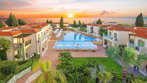 Un resort con piscina, lettini e vista sul mare al tramonto.