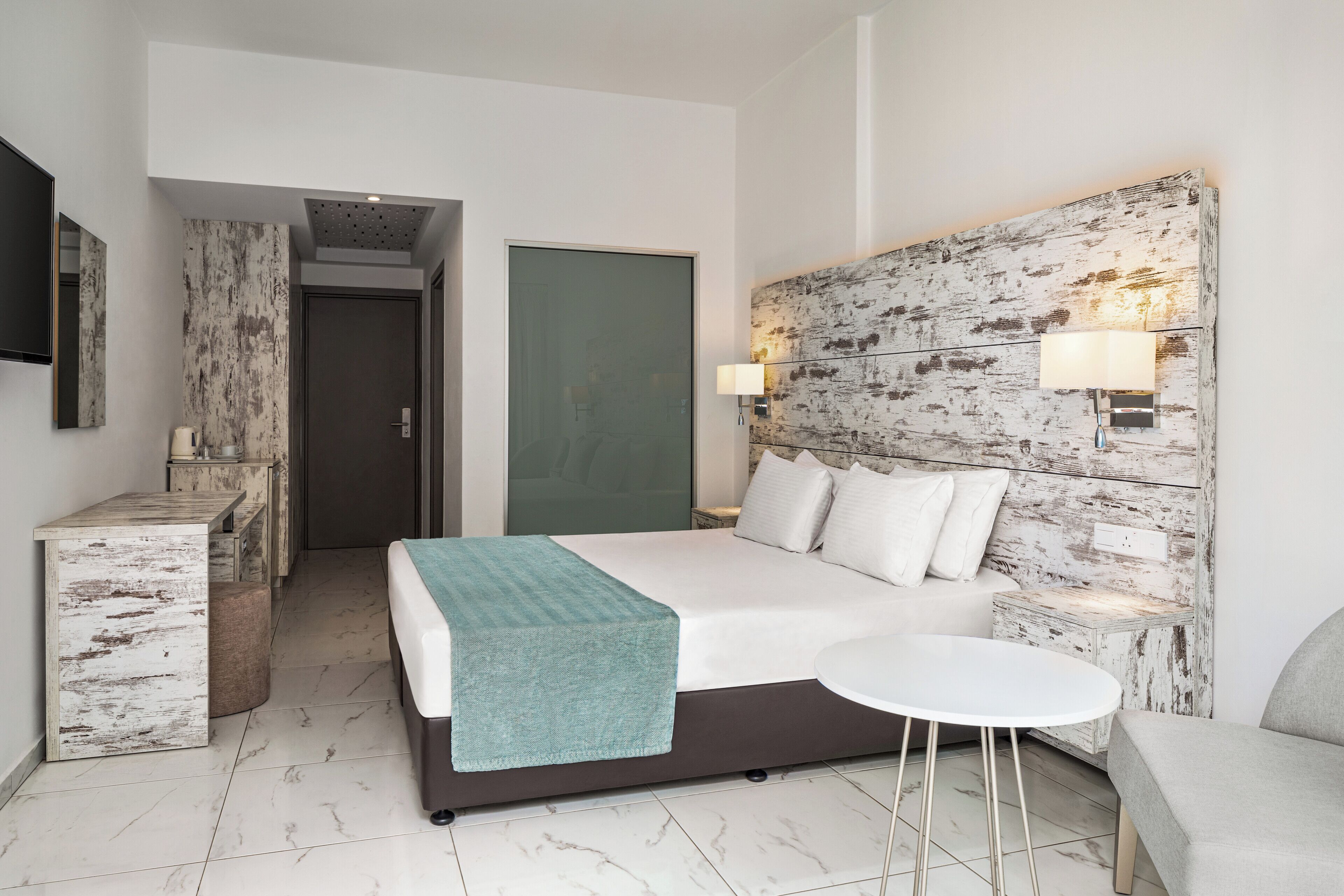 A modern hotel room with a bed, bedside table, lamp, and a small round table.