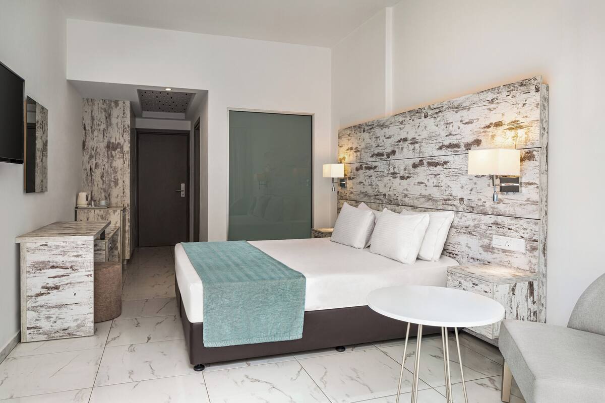 Una habitación de hotel moderna con cama, mesita de noche, lámpara y una pequeña mesa redonda.
