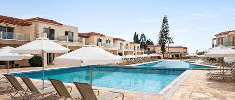 A pool area with lounge chairs and umbrellas, surrounded by buildings with balconies.