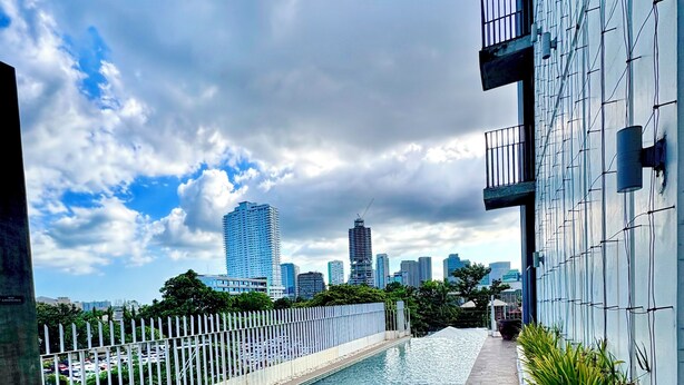 Una piscina en la azotea con vistas al horizonte de una ciudad, rodeada por una valla blanca y macetas con plantas.